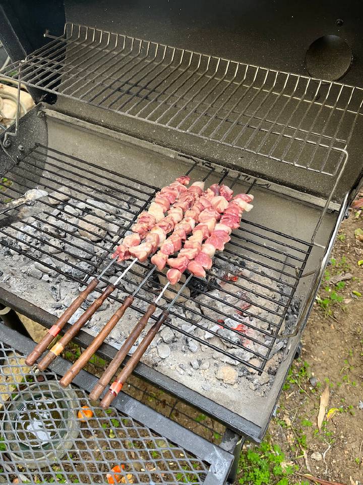 Skewers of meat cooking on an outdoor charcoal grill.