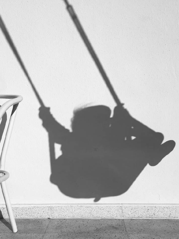 Shadow of a tiny person on a swing cast on a white wall.
