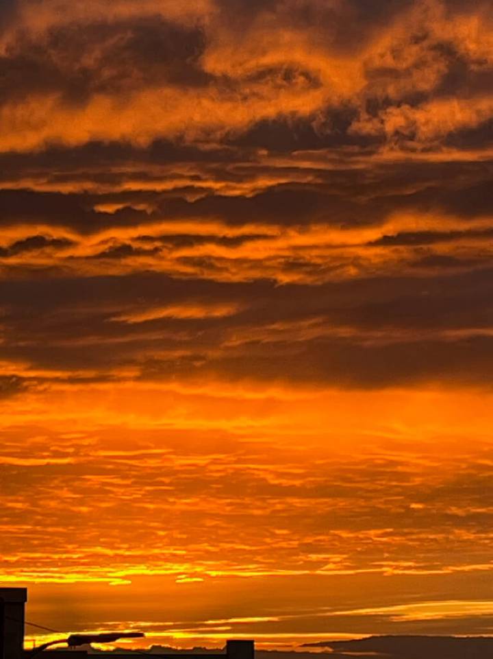 Sunrise with vibrant orange and yellow clouds over a silhouette of a city skyline.