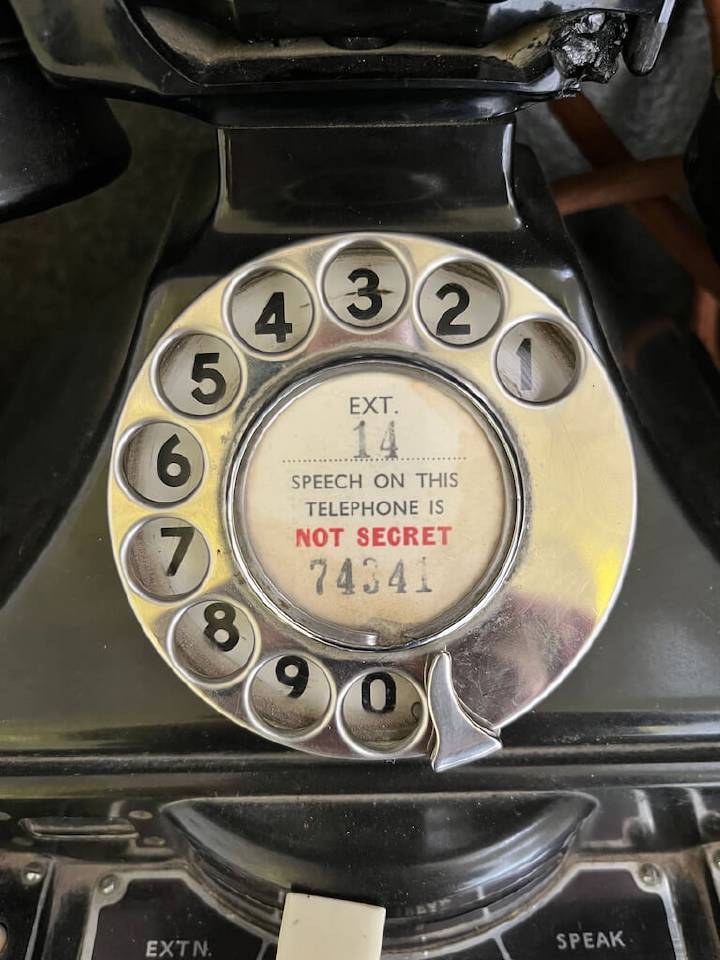 Close-up of a vintage rotary dial telephone with the message &quot;SPEECH ON THIS TELEPHONE IS NOT SECRET&quot; displayed in the centre.